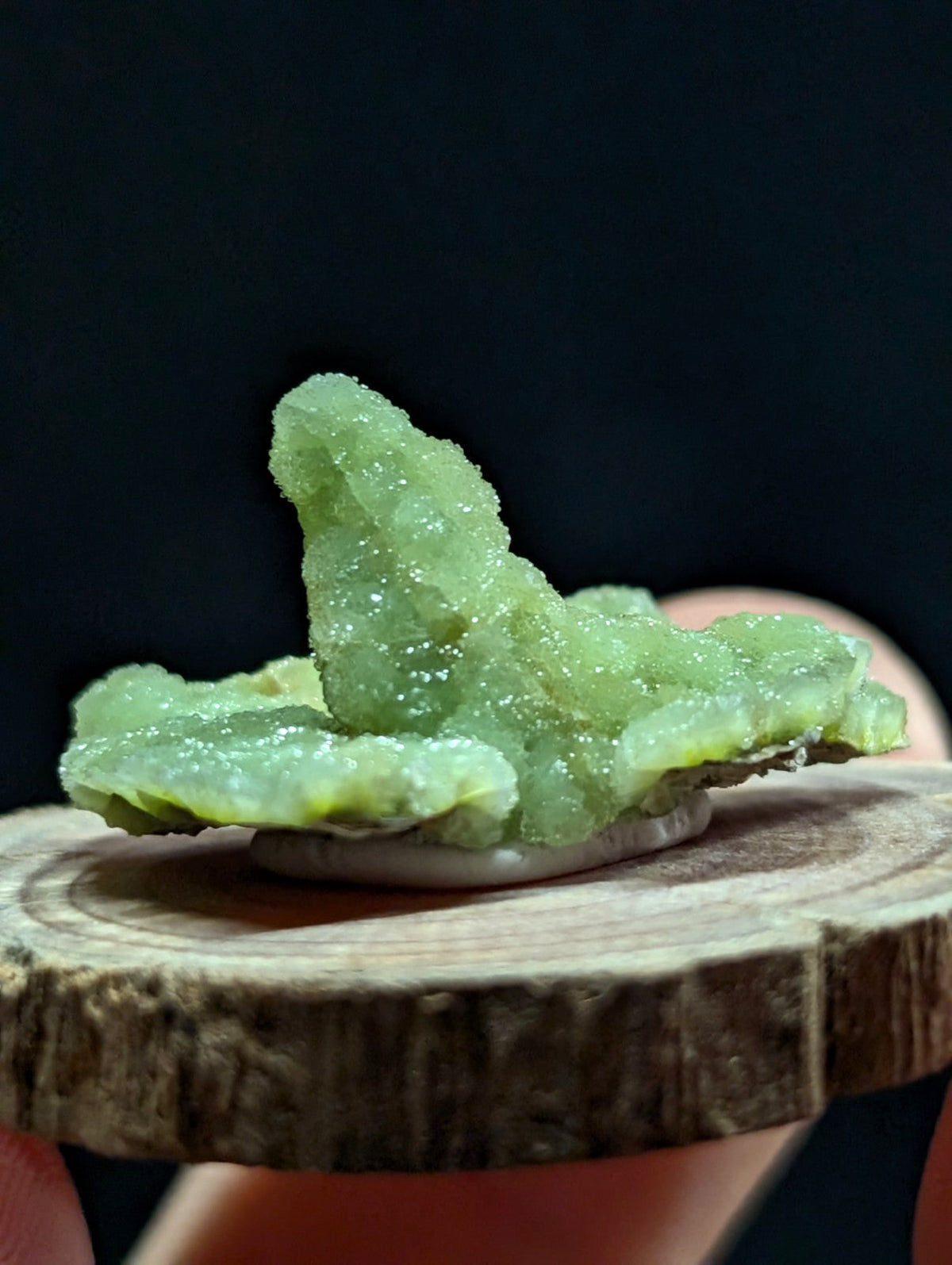 A translucent green crystal formation with a rough, jagged surface and sparkling facets.