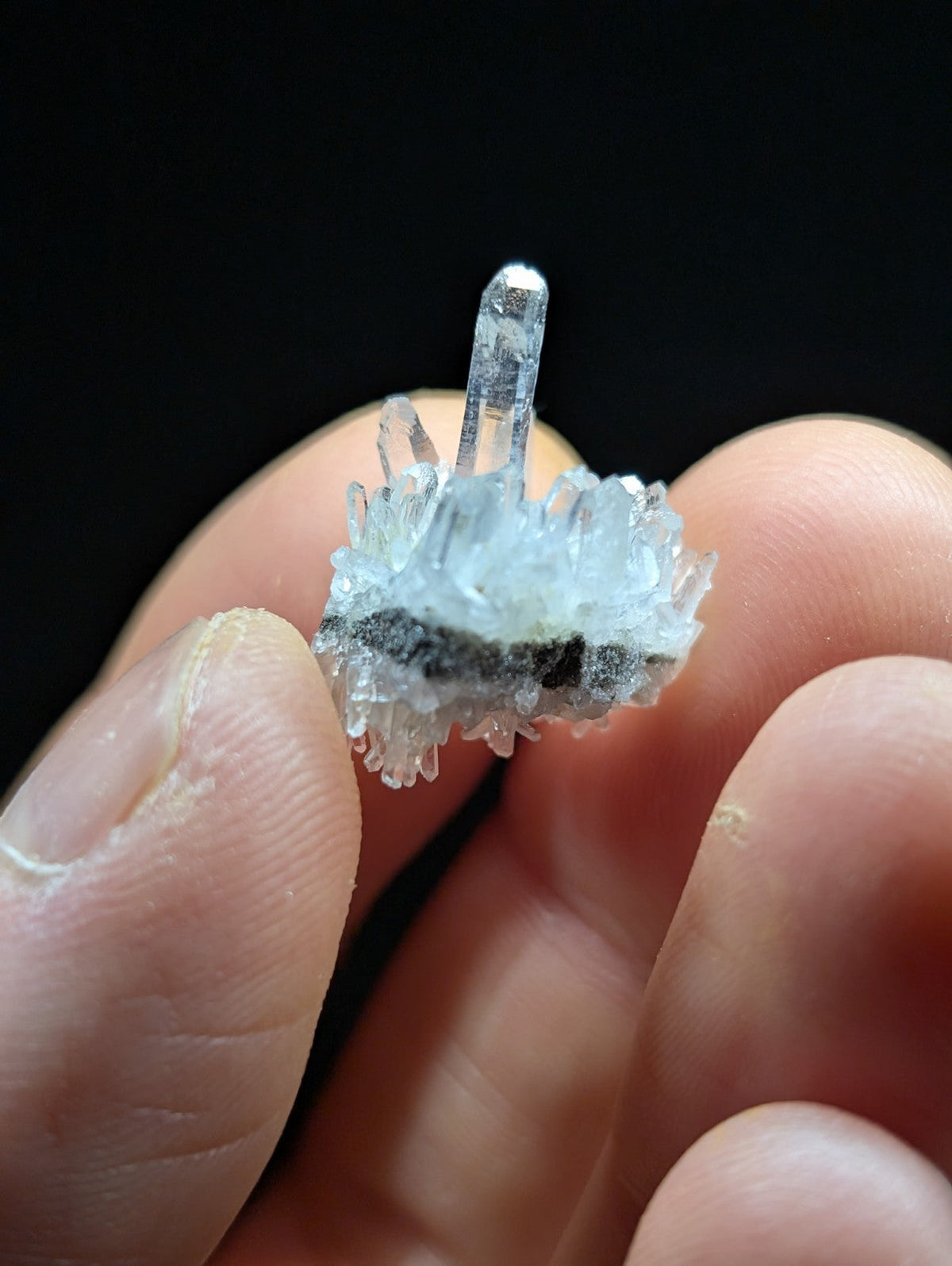 A translucent quartz crystal cluster with a central spike and radiating smaller crystals, held gently in someone’s fingers.