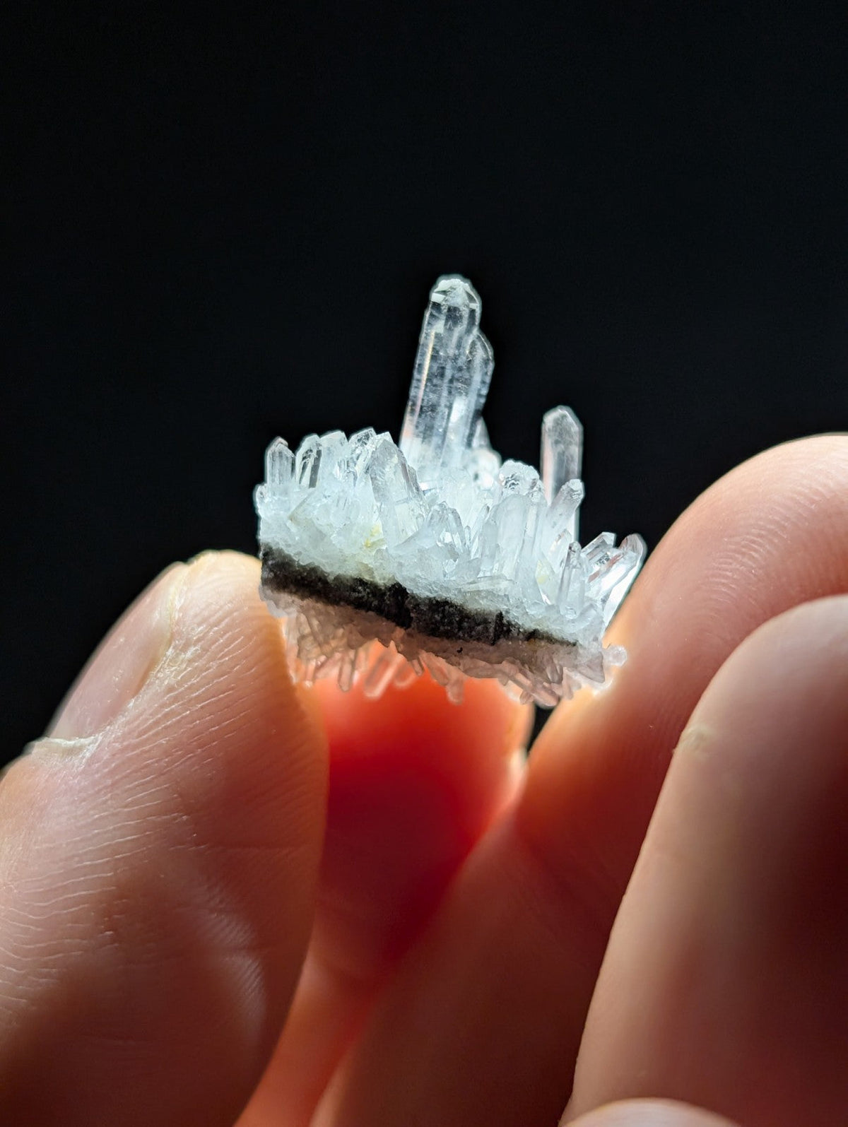 A translucent, clear quartz crystal cluster with sharp, pointed facets and a dark base.
