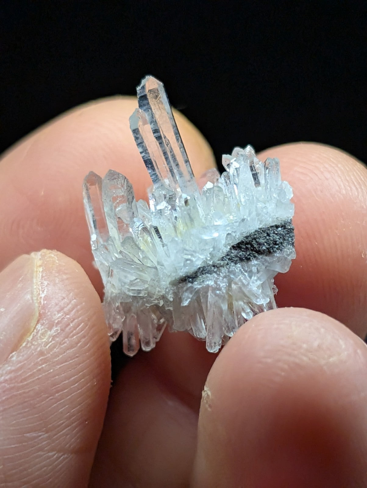 A clear, translucent quartz crystal cluster with sharp, pointed facets and a dark streak running through its center.