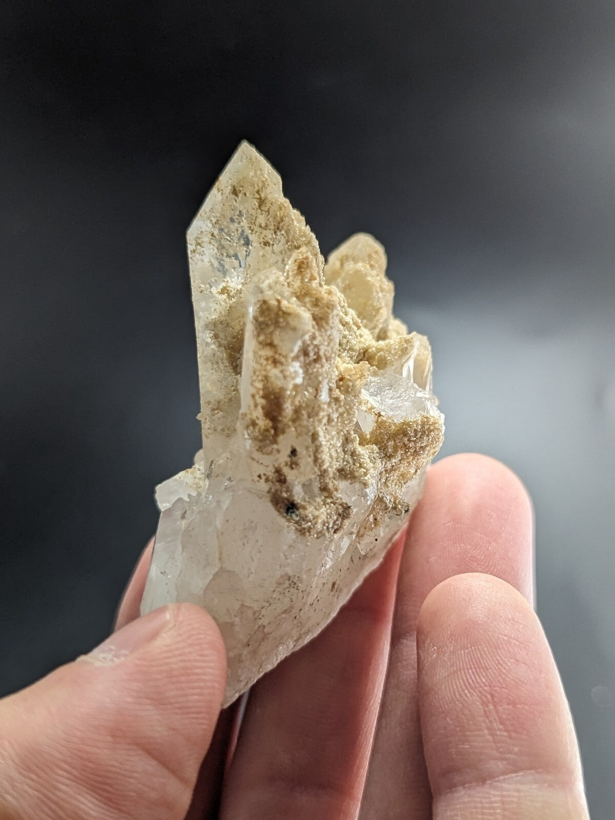 A translucent quartz crystal cluster with golden mineral inclusions, held gently between fingers.