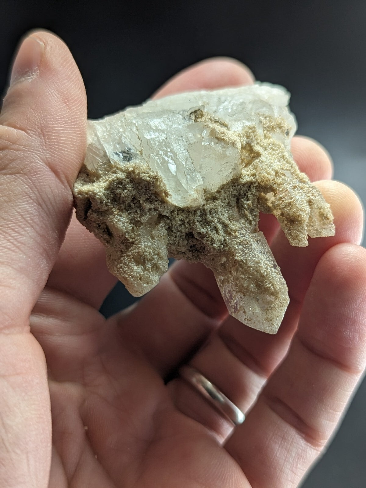 A translucent, pale quartz crystal cluster with rough, earthy matrix surrounding its clear, faceted points.