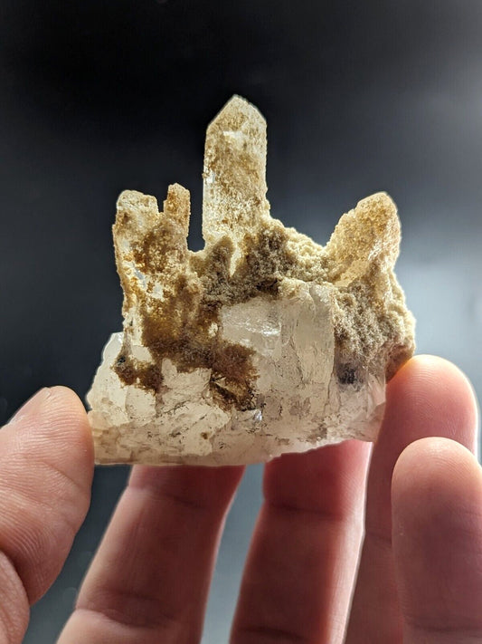A translucent quartz crystal cluster with a mix of clear and golden-brown mineral matrix, held gently between fingers.