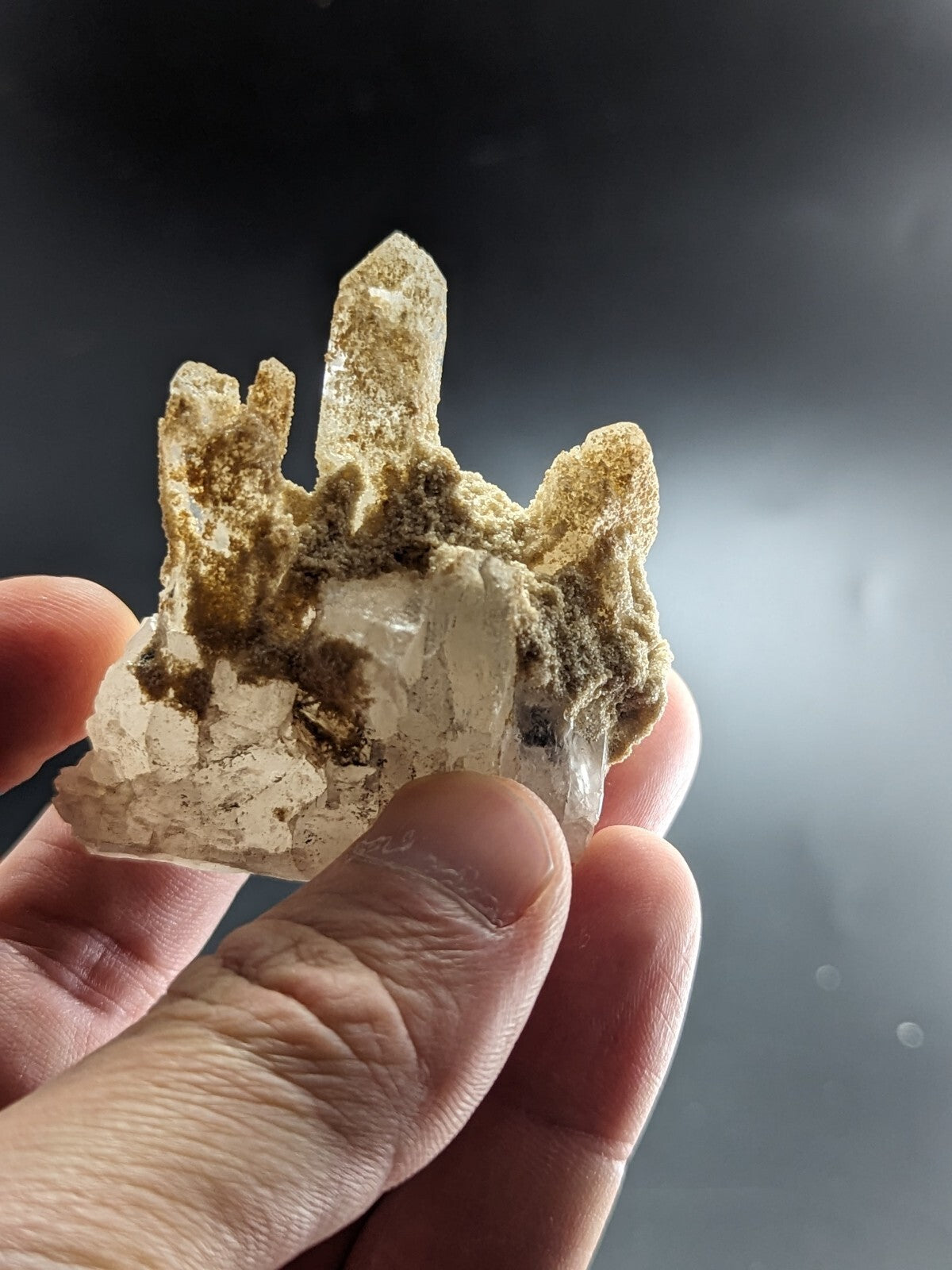 A translucent quartz crystal cluster with a central pointed spike and surrounding rough, earthy brown matrix.