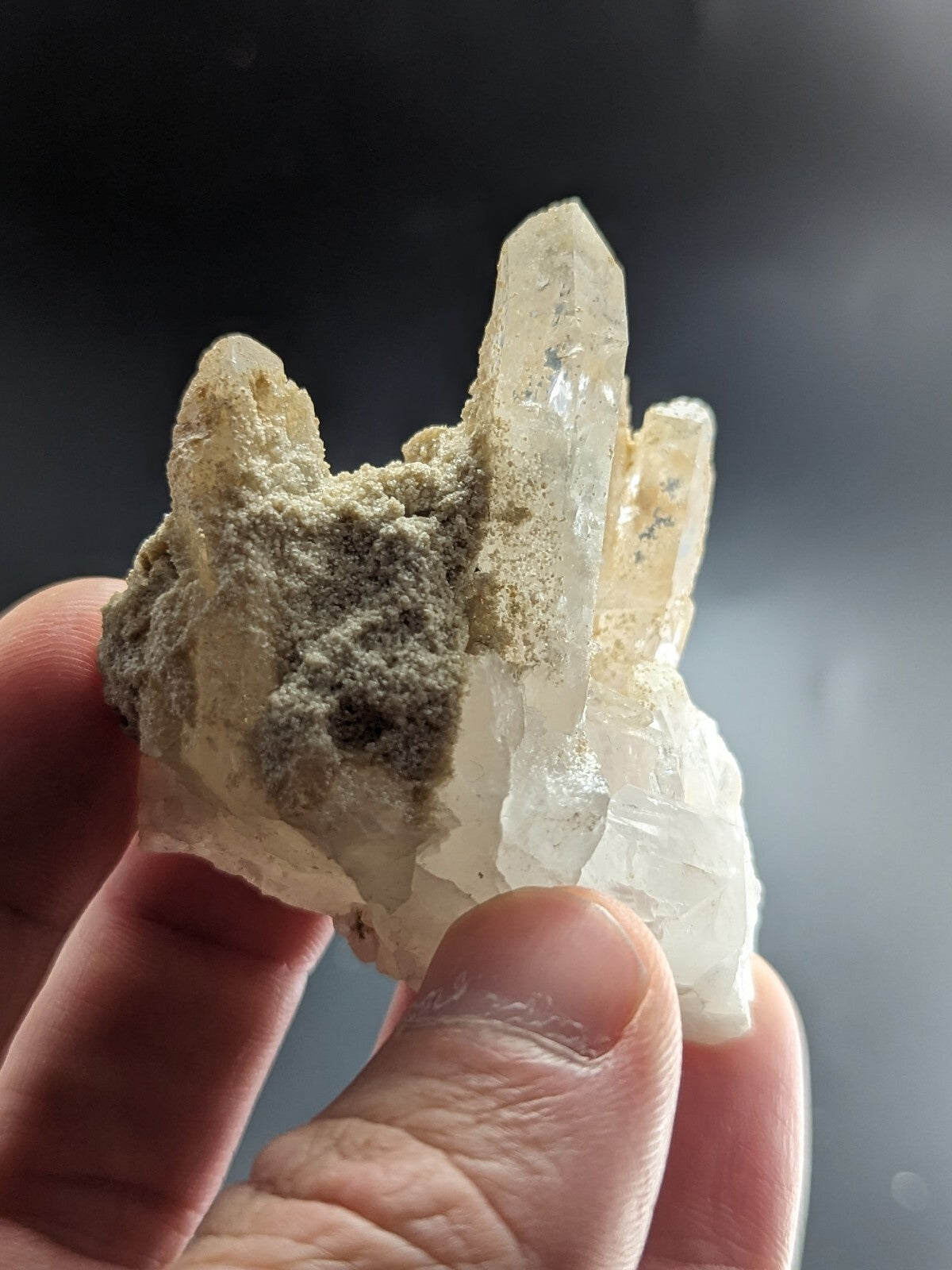 A translucent, pale quartz crystal cluster with sharp, pointed formations and a patch of grayish matrix material.