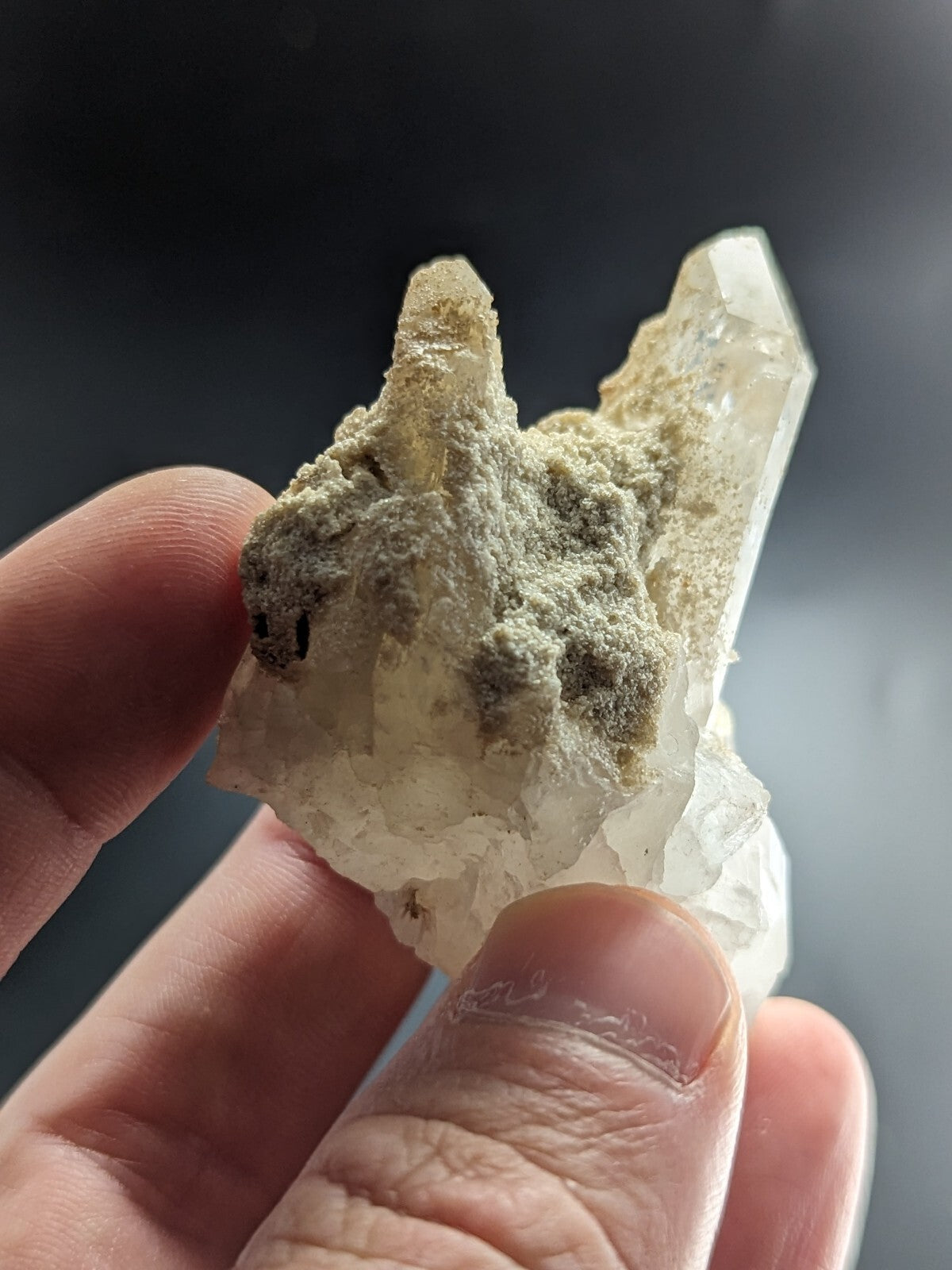 A translucent white quartz crystal cluster with a rough, mossy greenish-gray matrix.