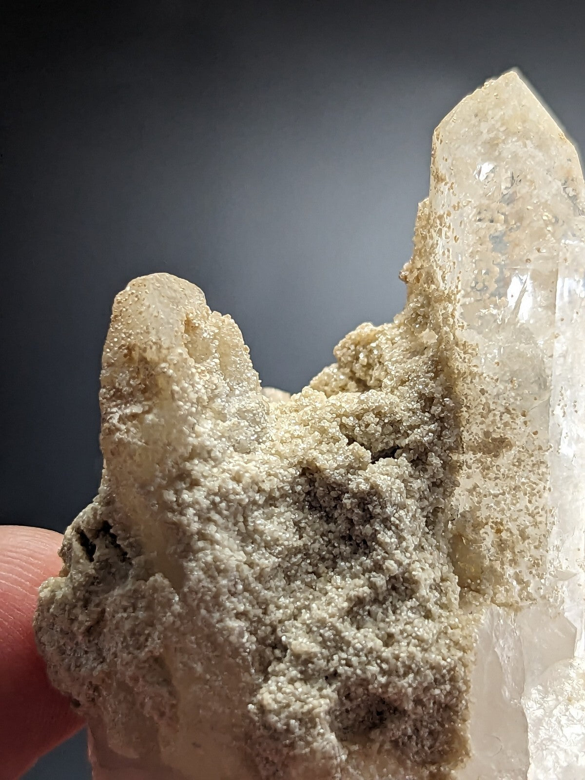 A translucent, pale quartz crystal cluster with a rough, textured matrix of earthy gray and white mineral deposits.