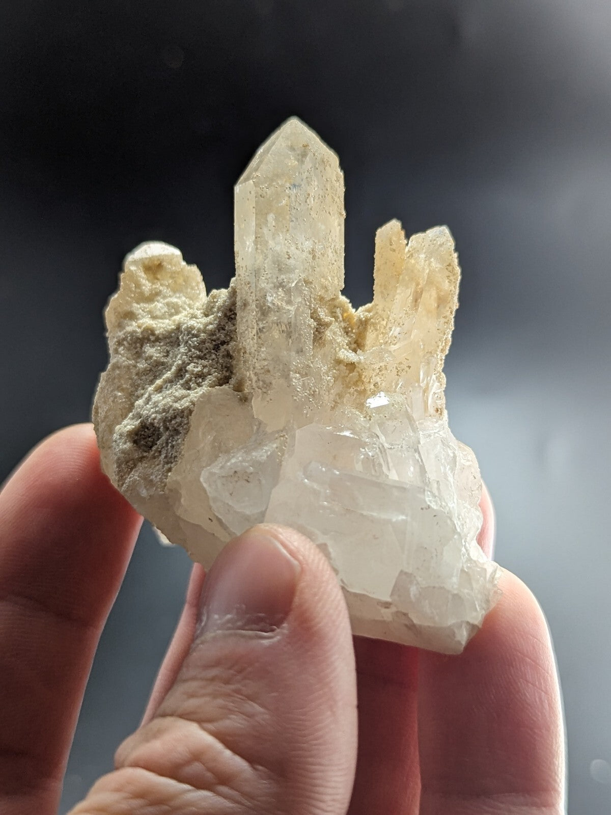 A translucent, pale quartz crystal cluster with a central pointed spike and surrounding rougher, textured formations.