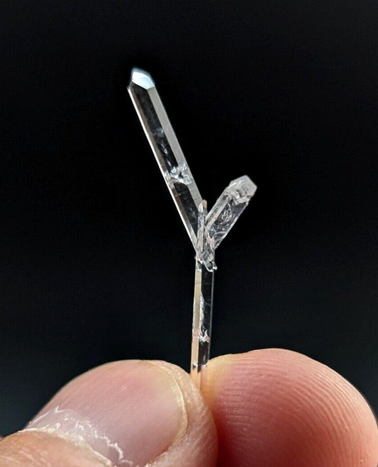 A clear, transparent quartz crystal with a distinct y-shaped formation and sharp, faceted edges.
