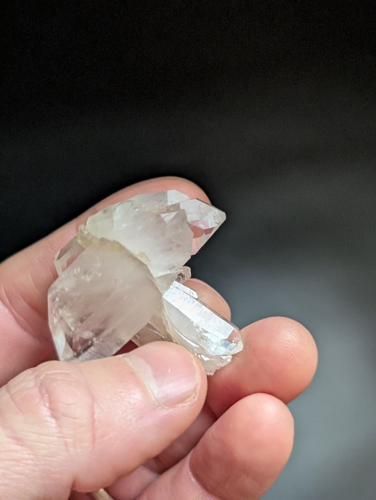 A cluster of clear, translucent quartz crystals held in a hand.