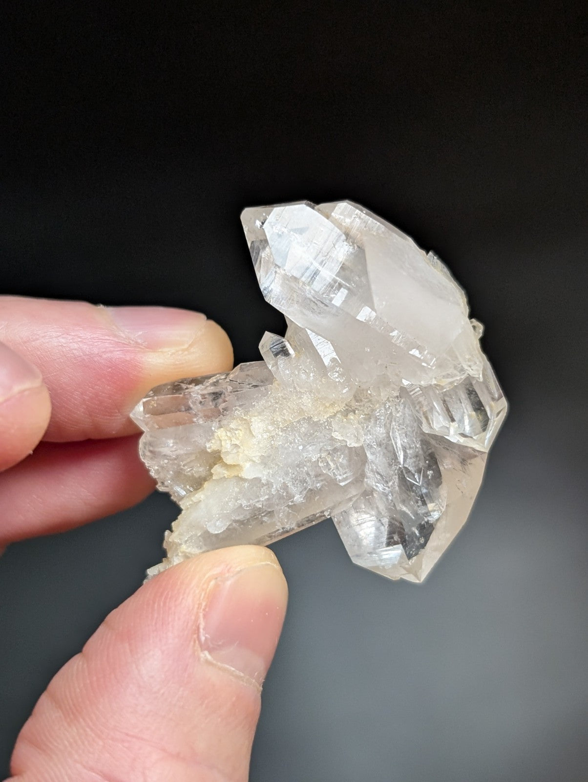 A translucent, clear quartz crystal cluster with sharp facets and a natural, earthy base.