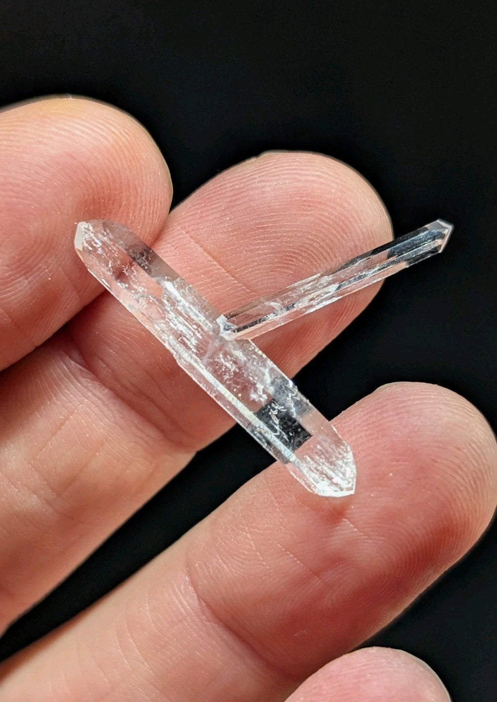 A clear quartz crystal cluster with two intersecting, faceted points held gently between fingers.