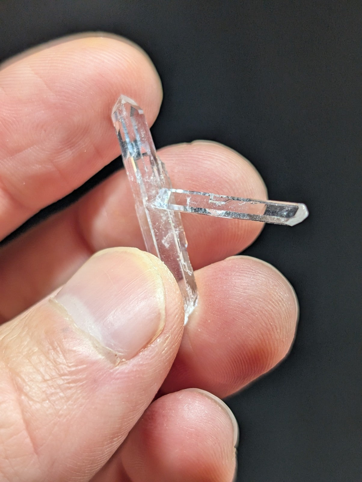 A clear, transparent quartz crystal with a distinct t-shaped formation and sharp, faceted edges.