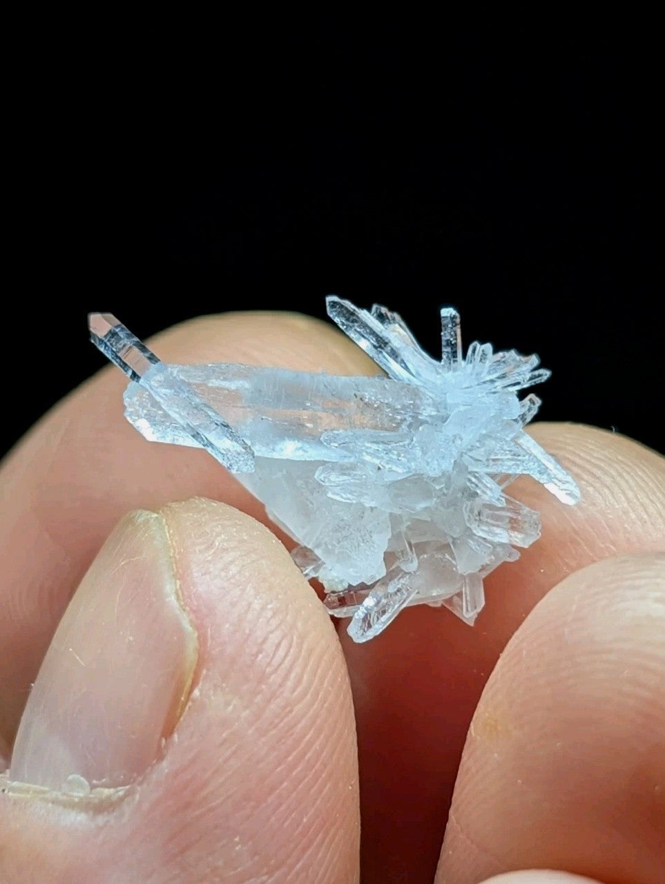 A delicate, translucent blue crystal cluster with sharp, interlocking facets held gently between fingers.