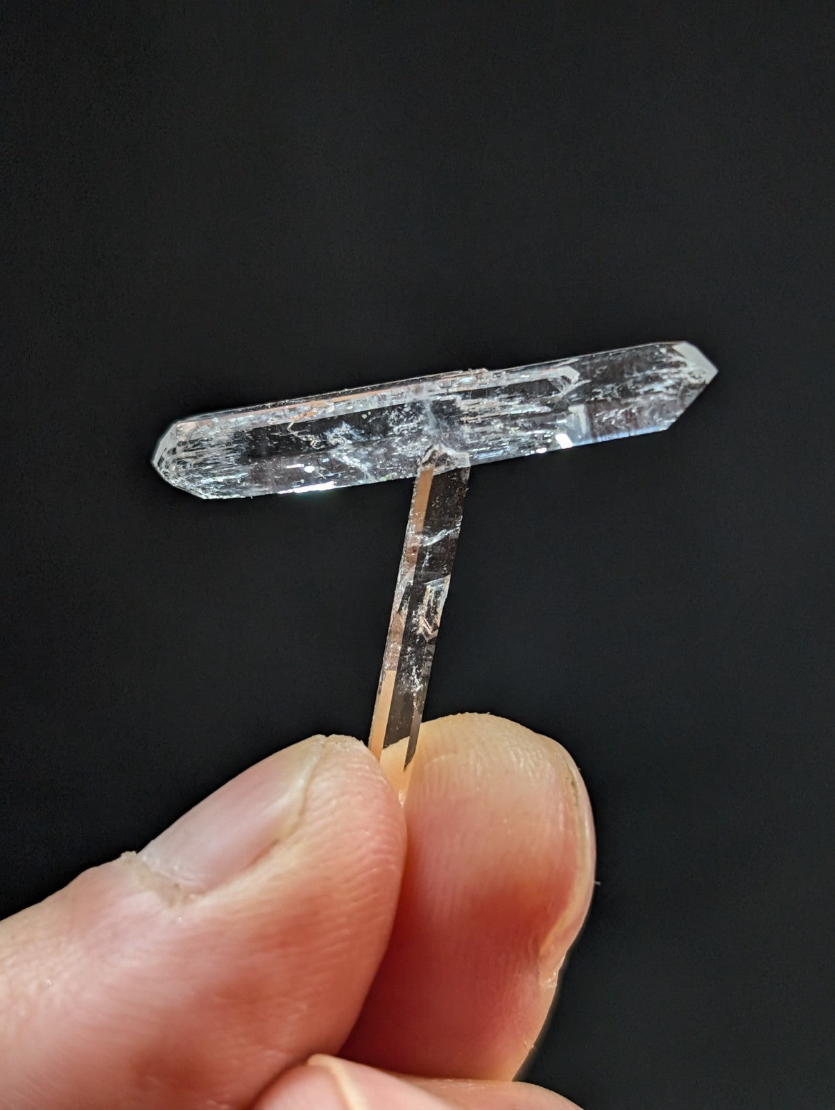 A clear, translucent quartz crystal with a distinct t-shaped formation and natural striations.