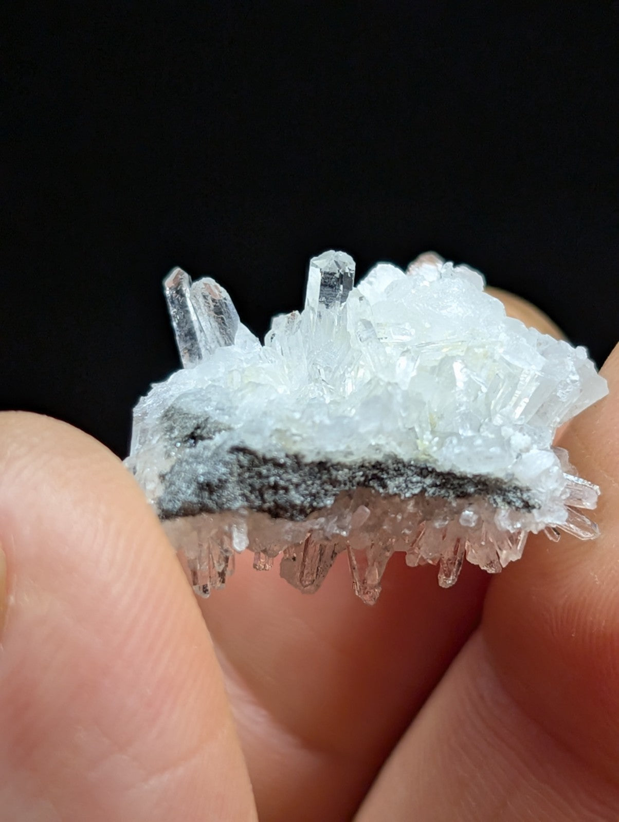 A translucent white crystal cluster with sharp, pointed facets and a dark gray mineral base.