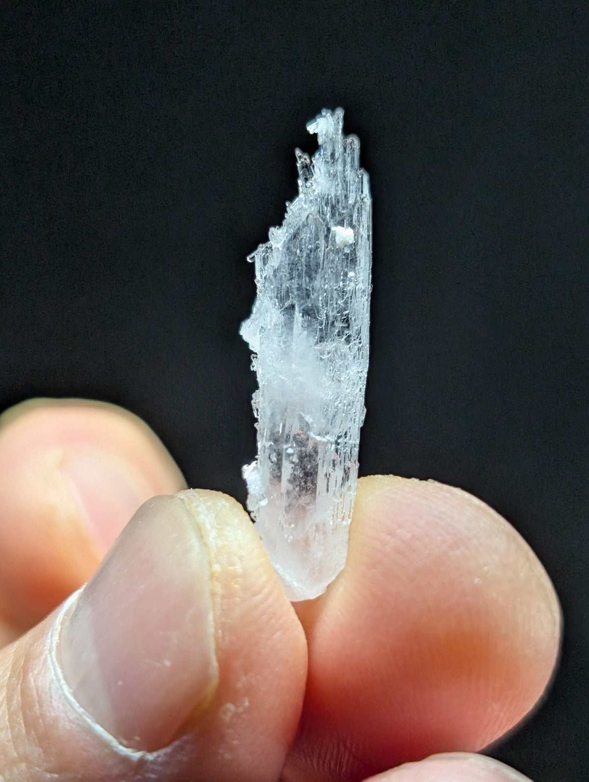 A translucent, crystalline mineral specimen with a jagged, elongated form and visible internal striations.