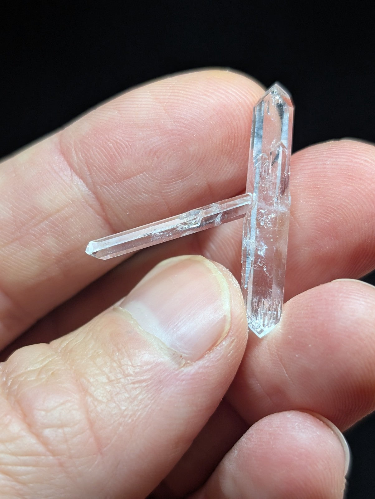 A clear quartz crystal cluster with two distinct, transparent prisms held gently between fingers.