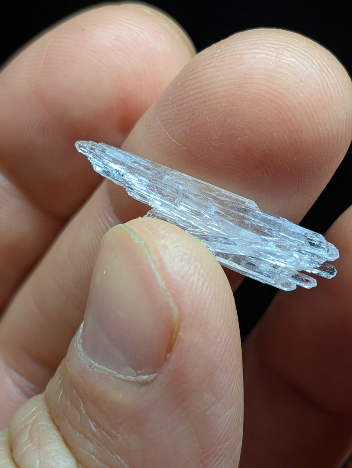 A translucent, icy-blue crystal with a jagged, layered structure held delicately between fingers.