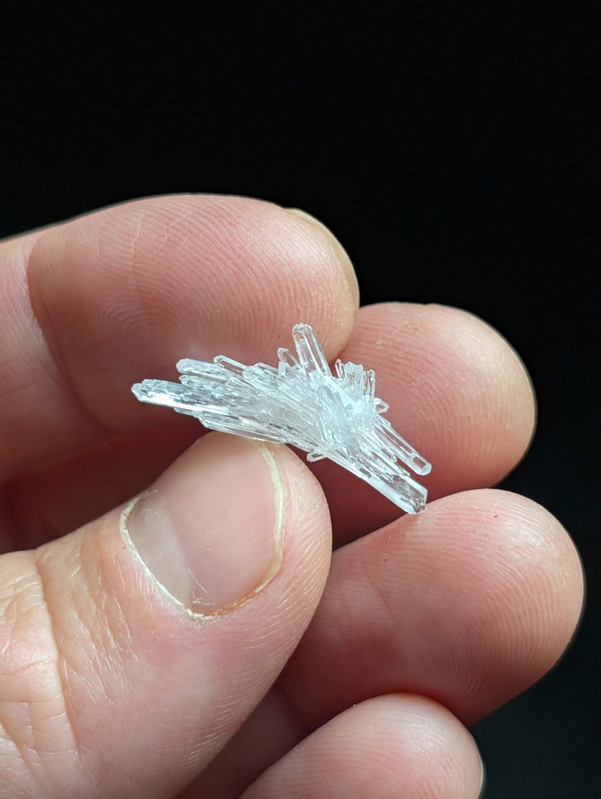 A delicate, translucent crystal cluster with sharp, interlocking facets held gently between fingers.