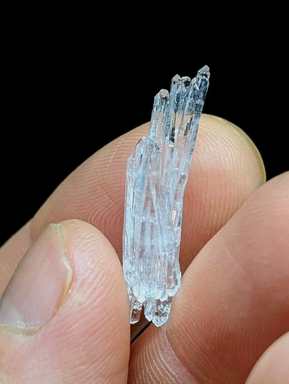 A delicate cluster of translucent blue quartz crystals, held gently between fingers.