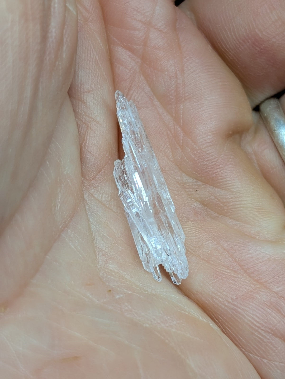 A translucent, crystalline mineral specimen with jagged edges and a pointed tip rests in the palm of a hand.