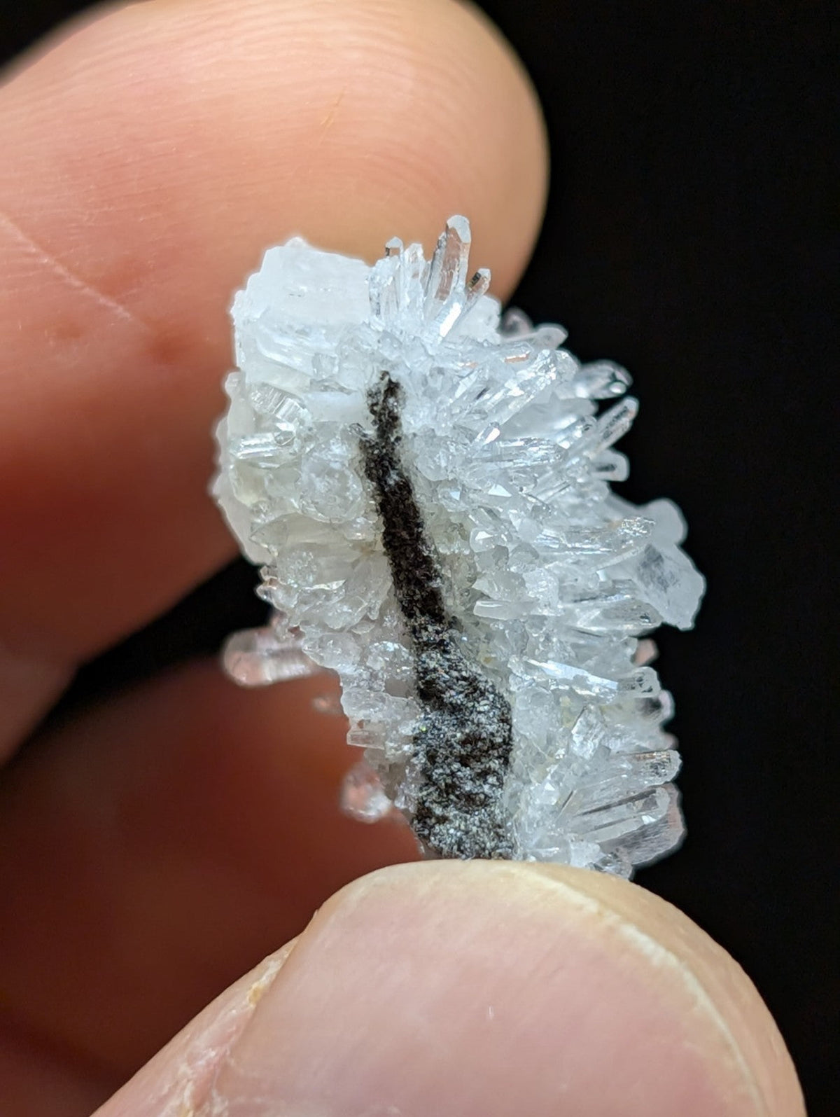 A translucent, crystalline mineral specimen with sharp, jagged facets and a central dark streak running through its structure.