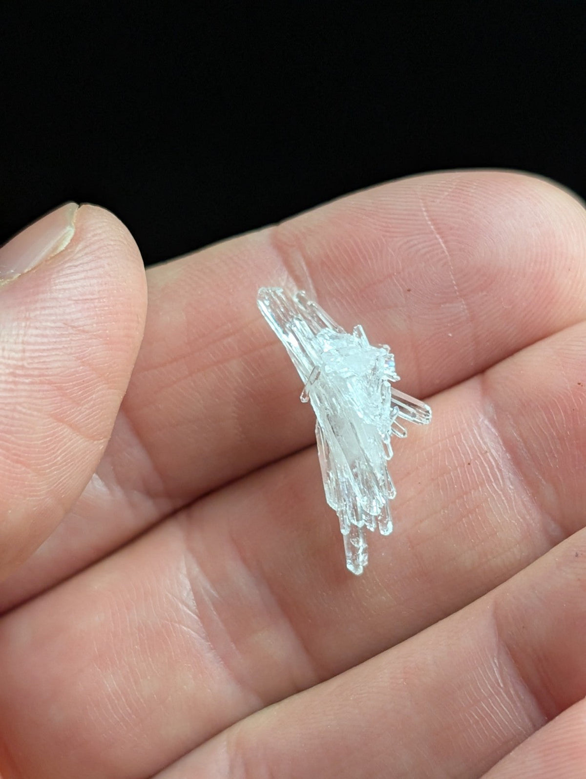 A delicate, translucent blue crystal cluster with sharp, interlocking facets rests gently in the palm of a hand.