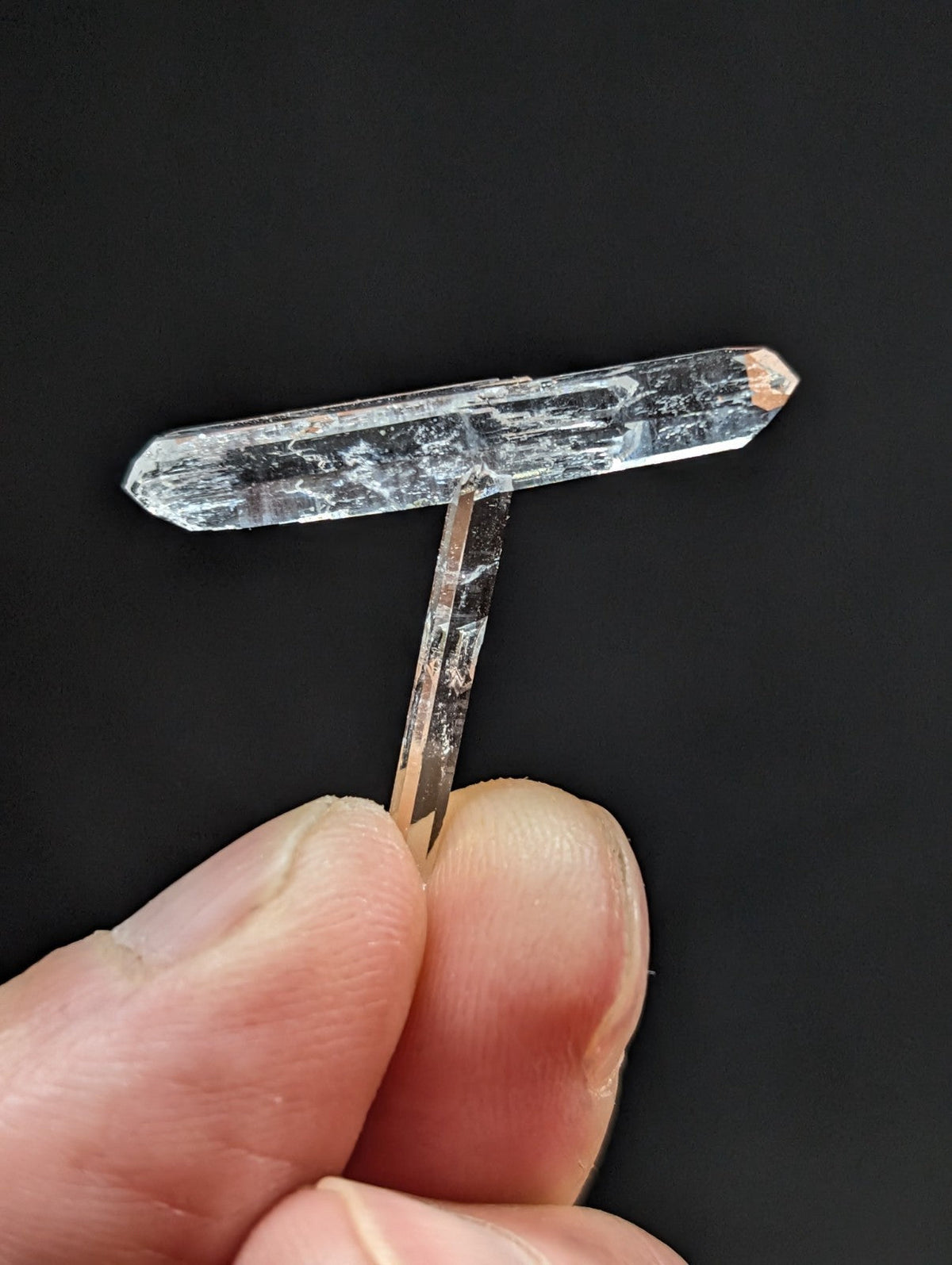 A clear, translucent quartz crystal with a t-shaped structure and natural striations.