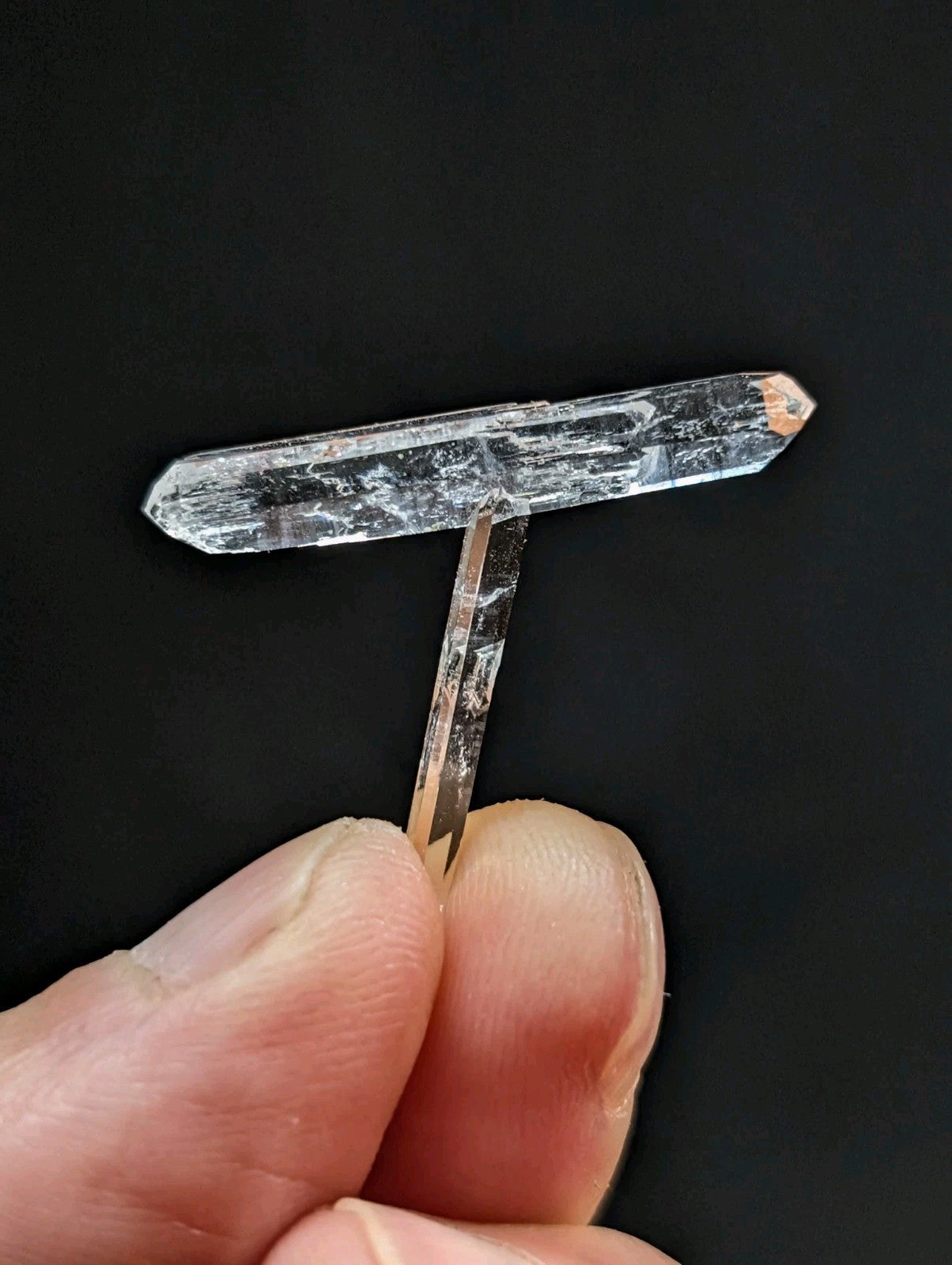 A clear, translucent quartz crystal with a t-shaped structure and natural internal striations.