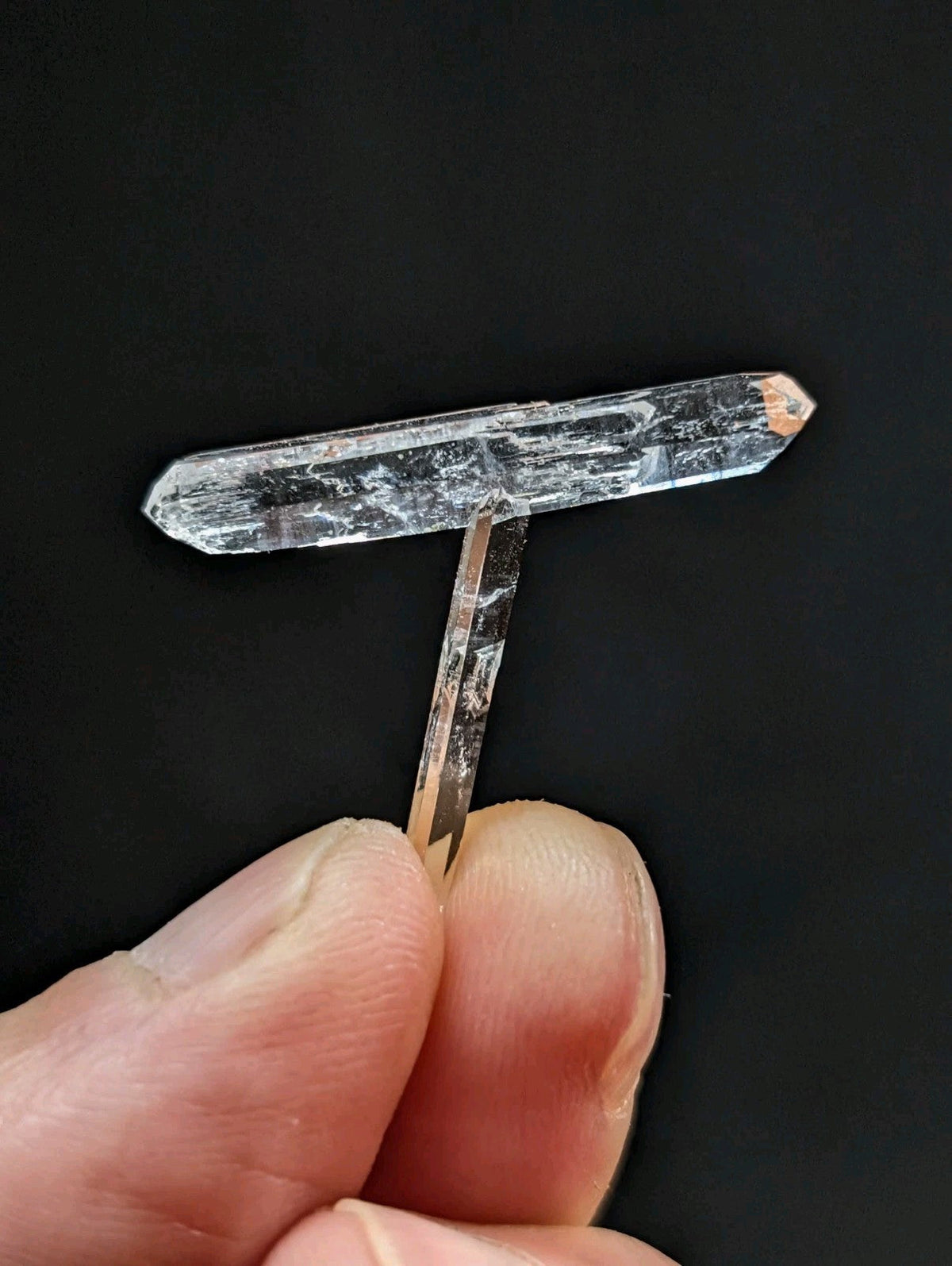 A clear, translucent quartz crystal with a t-shaped structure and natural internal striations.