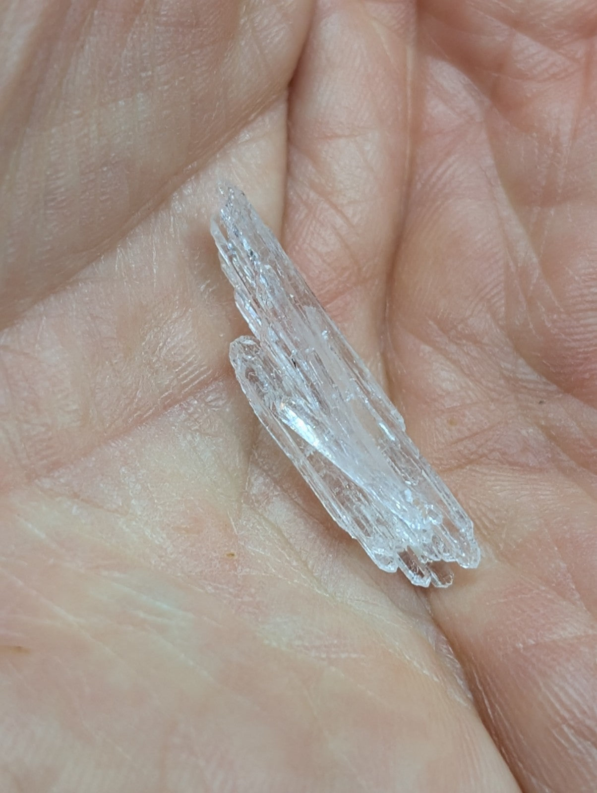 A translucent, clear crystal with jagged edges and a pointed tip rests in the palm of a hand.