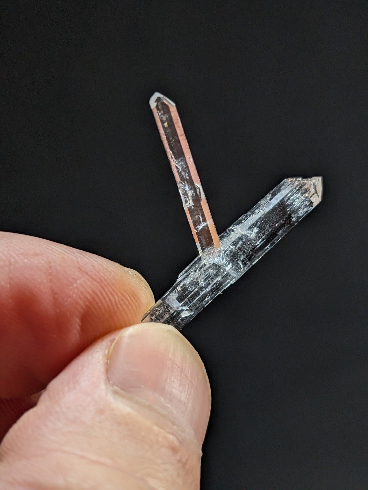 Two translucent quartz crystals, one with a subtle pinkish hue and the other clear, held delicately between fingers.