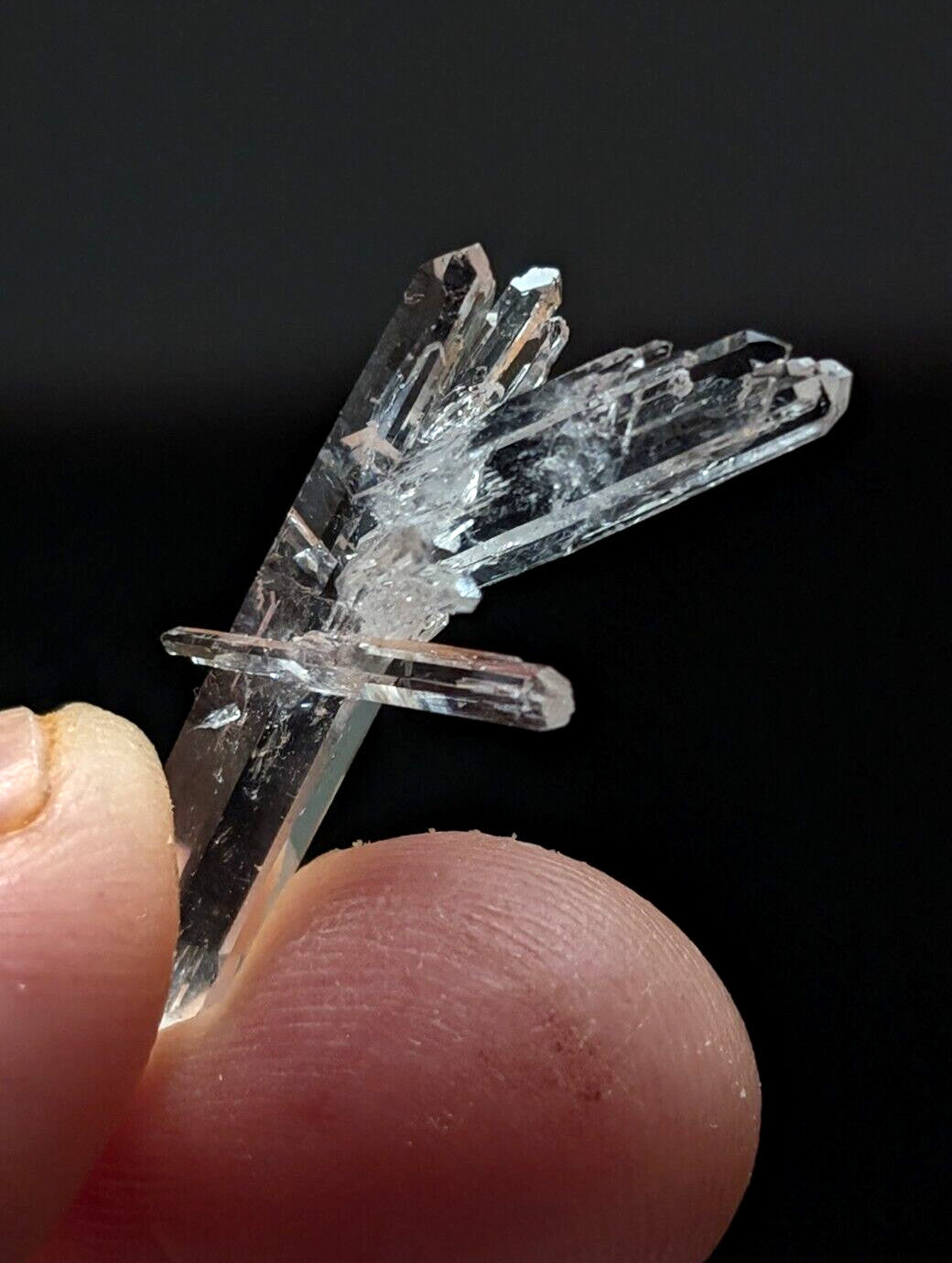 A clear quartz crystal cluster with multiple transparent, faceted points held between fingers.