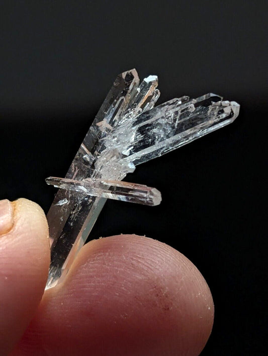 A clear quartz crystal cluster with multiple transparent, faceted points held between fingers.