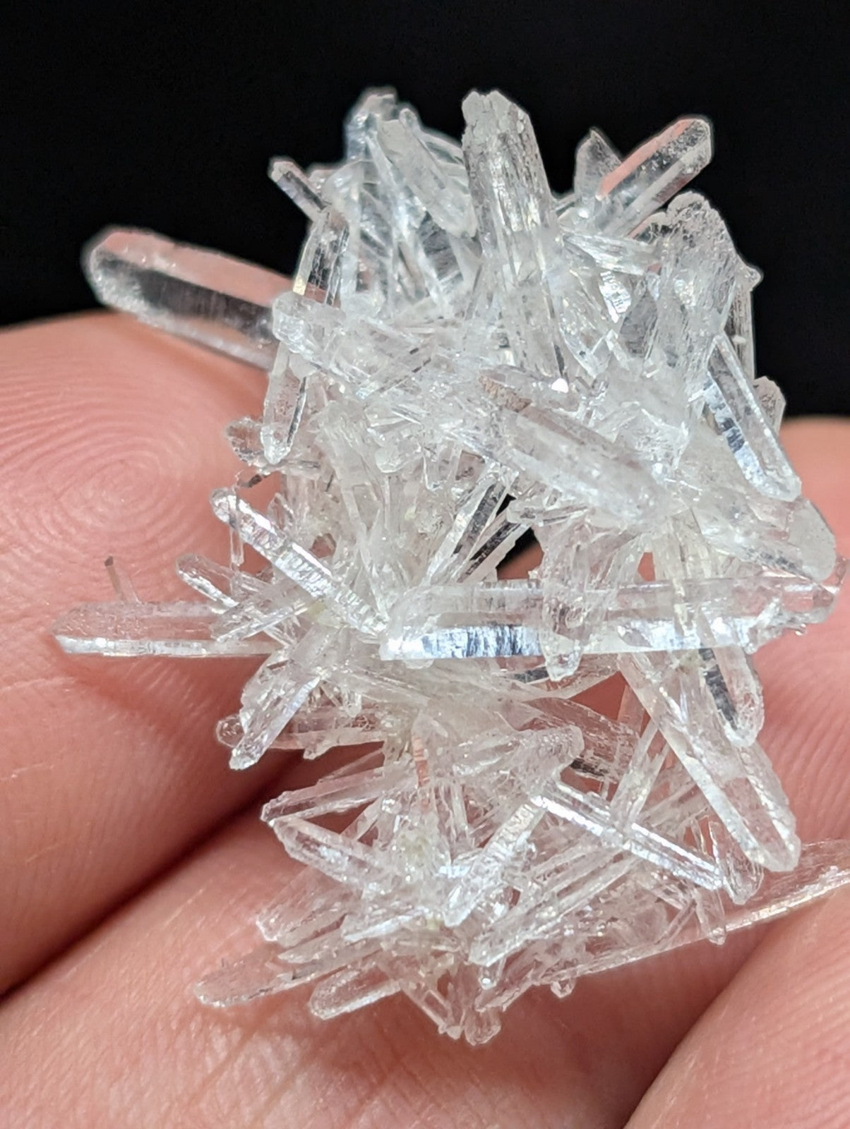 A cluster of transparent, faceted quartz crystals held in a hand.