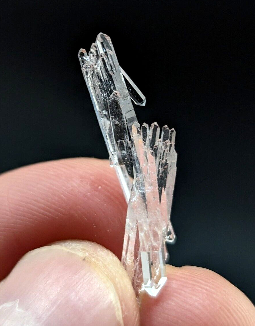 A cluster of transparent, faceted quartz crystals held between fingers.