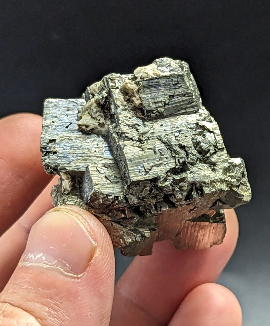 A hand holds a rough, metallic greenish-gray mineral specimen with distinct crystalline facets and layered textures.