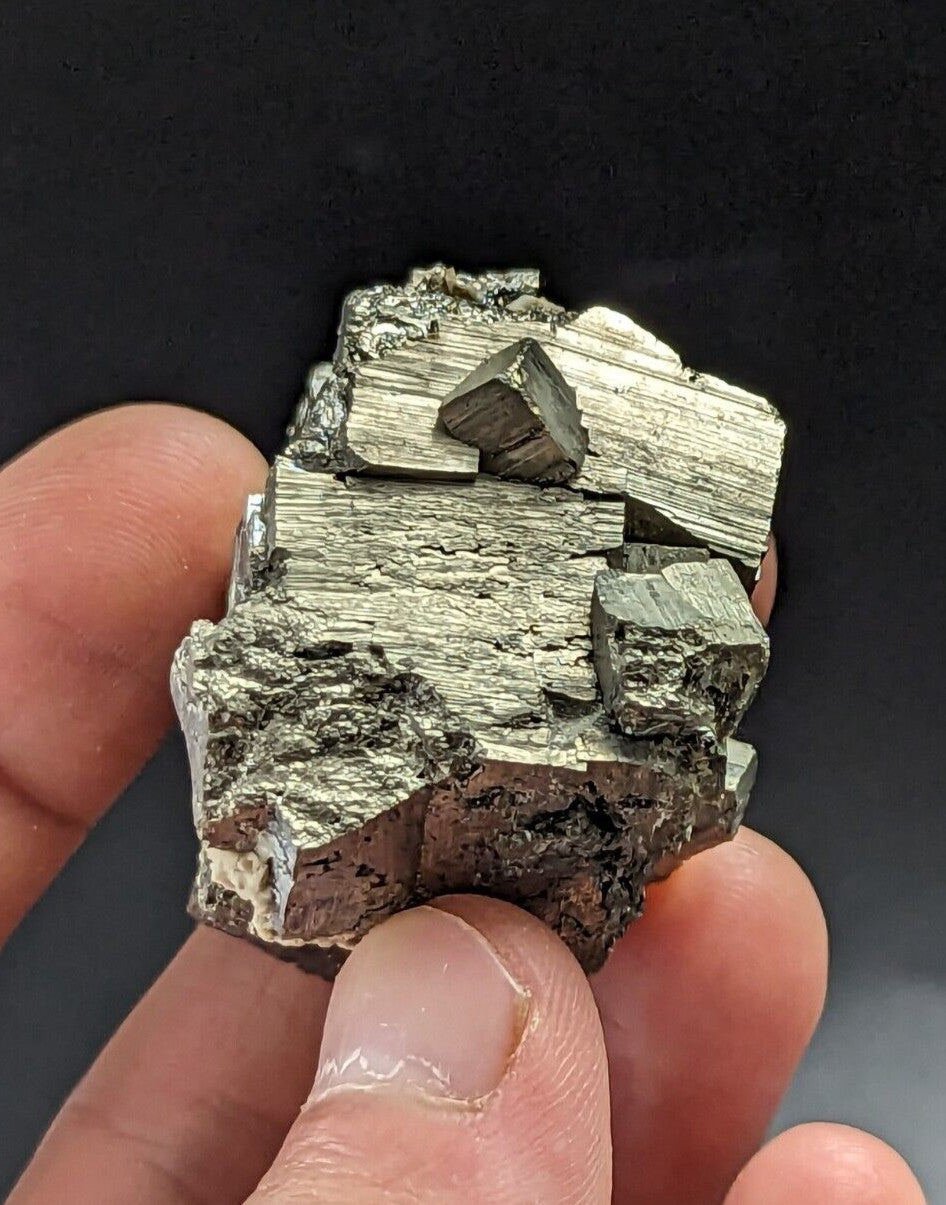 A hand holds a cluster of metallic, silver-gray pyrite crystals with distinct geometric facets and rough, earthy textures.