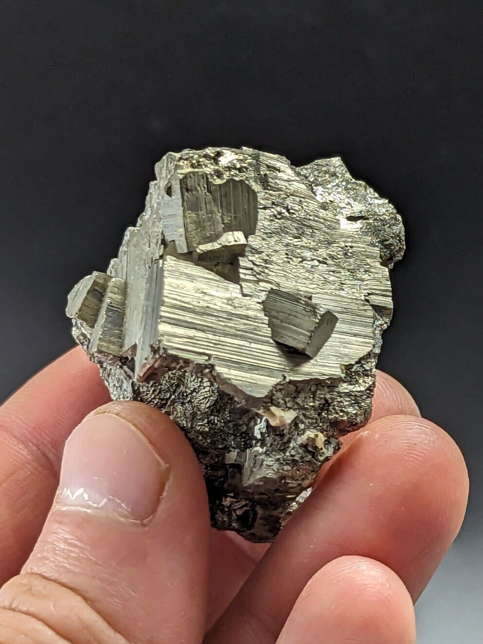 A hand holds a rough, irregularly shaped specimen of pyrite with metallic golden-yellow crystals embedded in a darker matrix.
