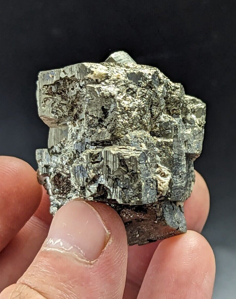 A rough, metallic greenish-gray mineral specimen with distinct crystalline facets and a slightly uneven surface.