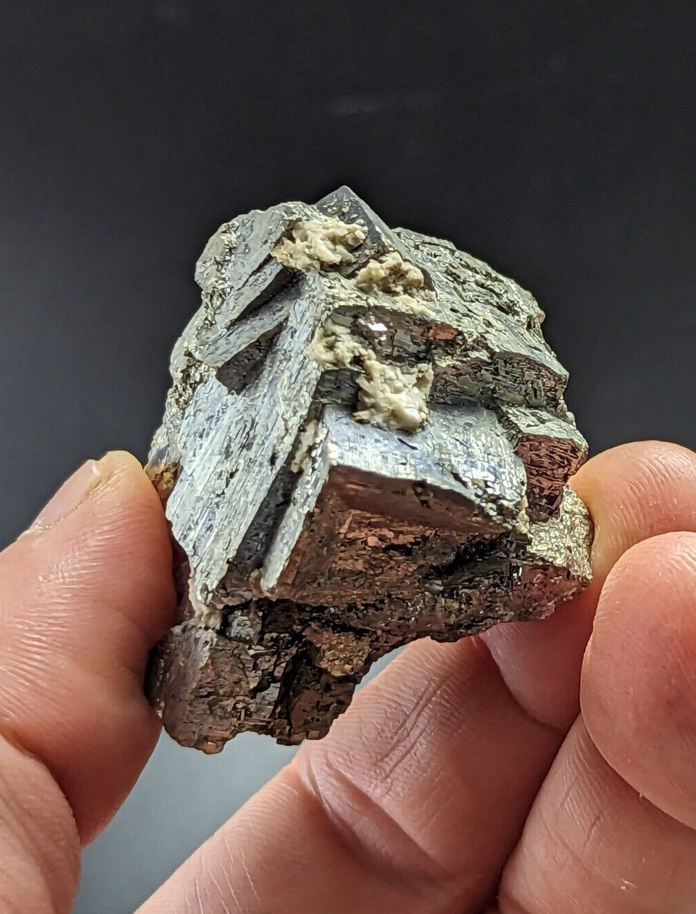 A rough, irregularly shaped mineral specimen with a mix of dark gray and reddish-brown hues, featuring distinct crystalline facets and patches of lighter greenish material.