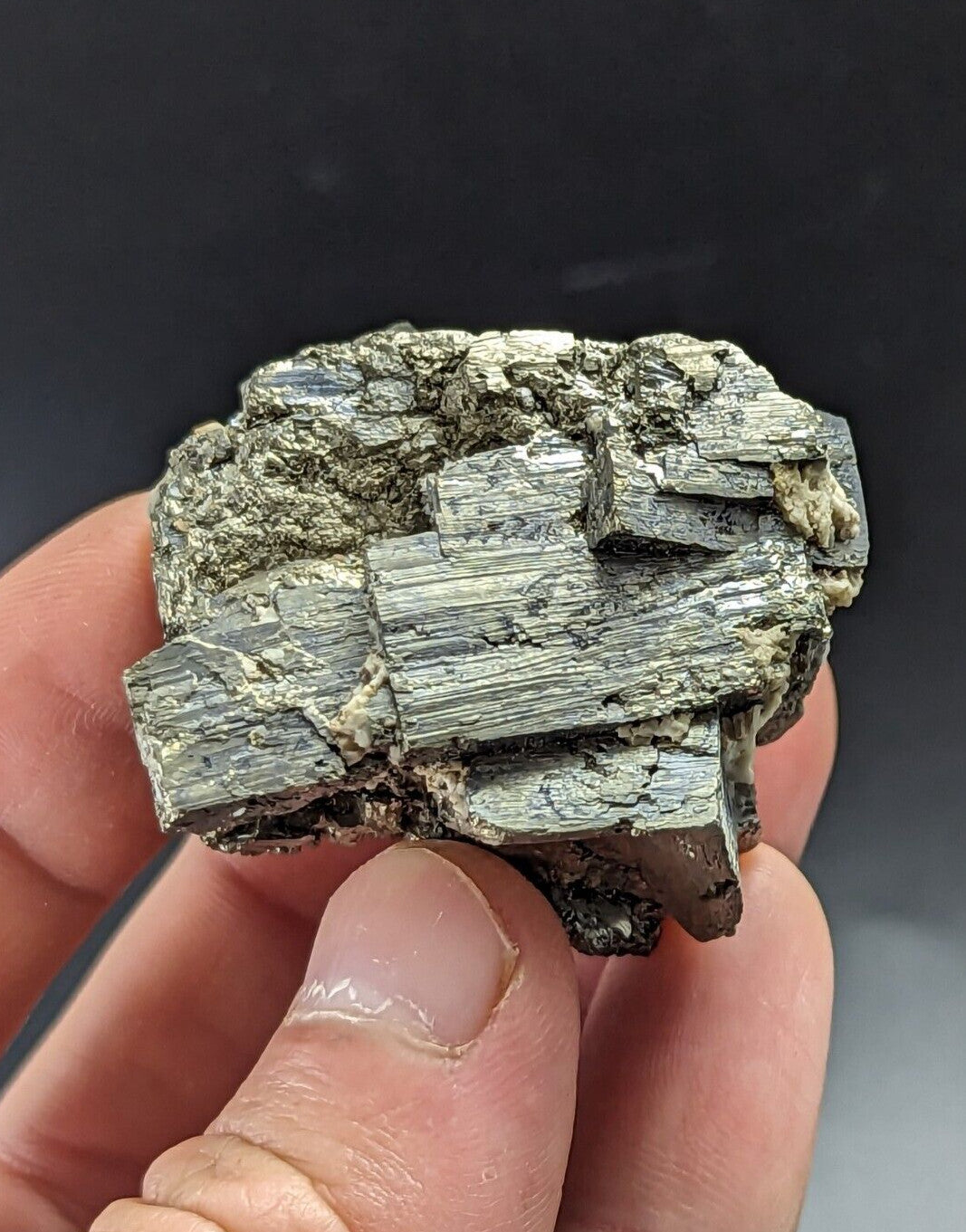 A hand holds a rough, grayish-green mineral specimen with distinct layered and crystalline textures.