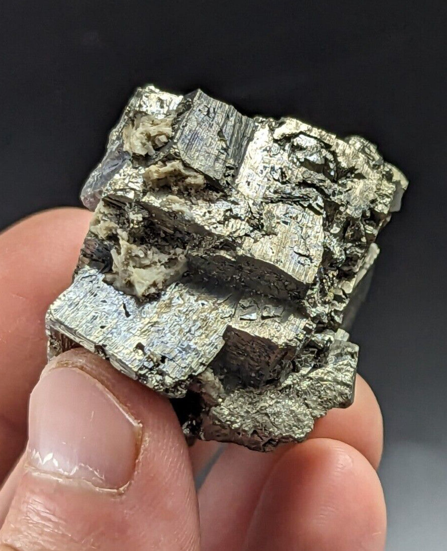 A hand holds a metallic, silver-gray pyrite crystal cluster with jagged edges and rough, textured surfaces.