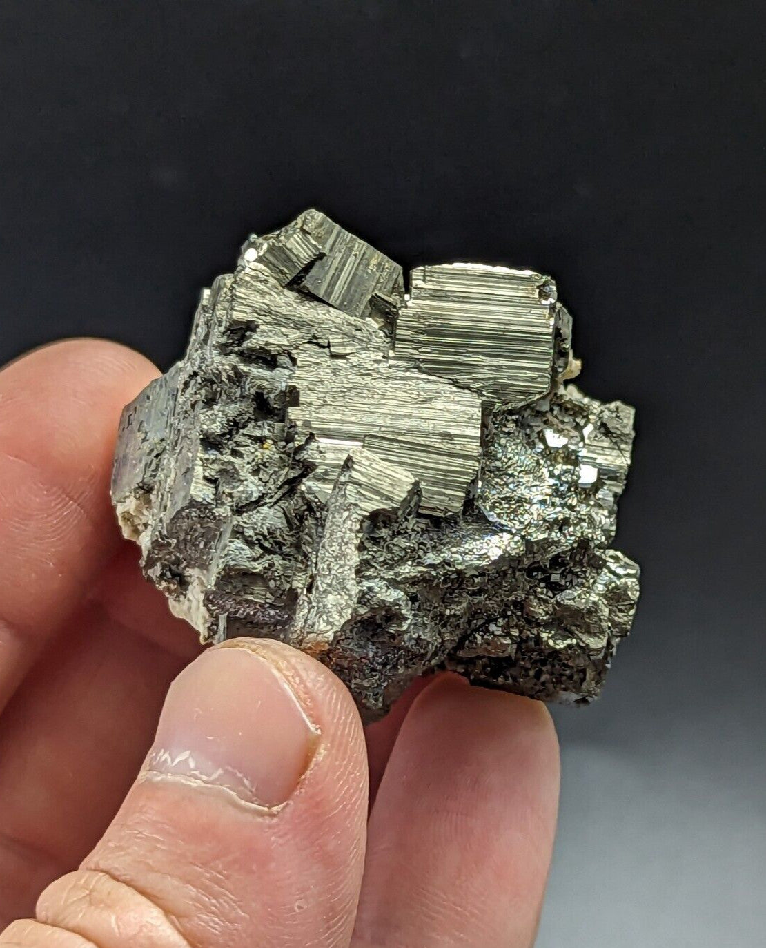 A metallic, silver-gray pyrite crystal cluster with distinct striations and a rough, jagged surface.