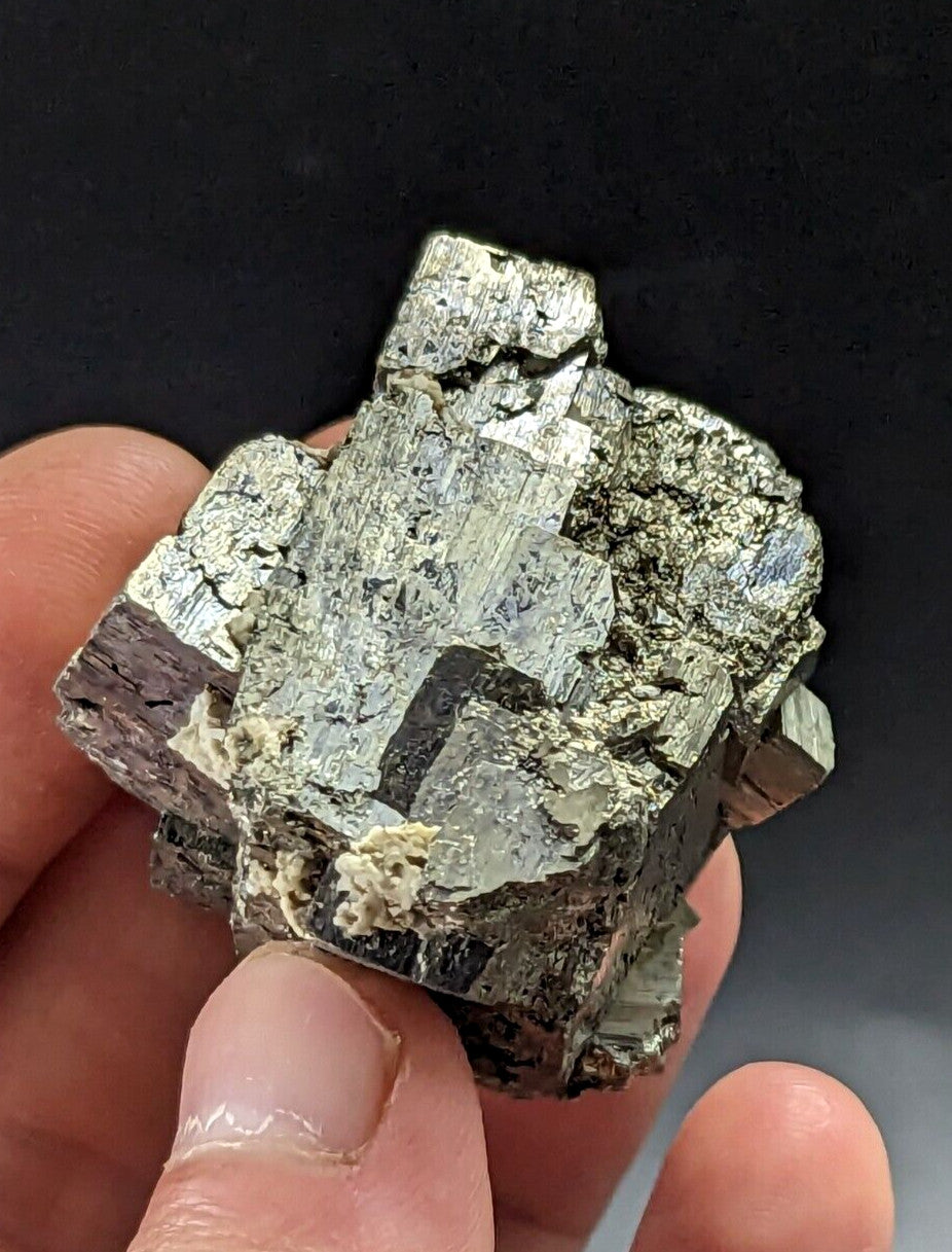 A hand holds a metallic, silver-gray pyrite crystal cluster with jagged edges and reflective facets.