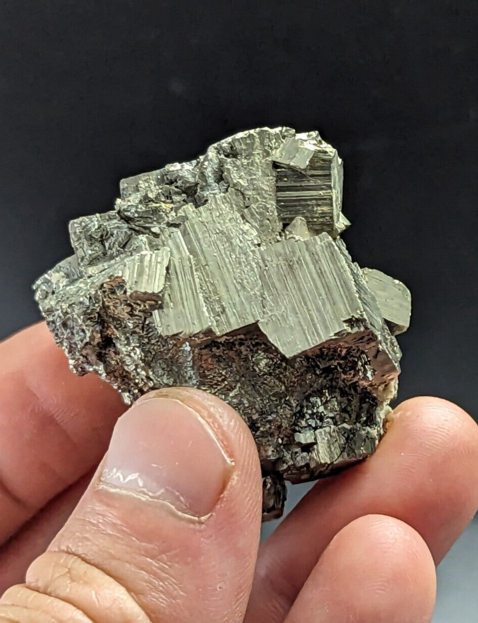 A cluster of metallic, greenish-gray pyrite crystals with distinct striations and a rough, jagged surface.