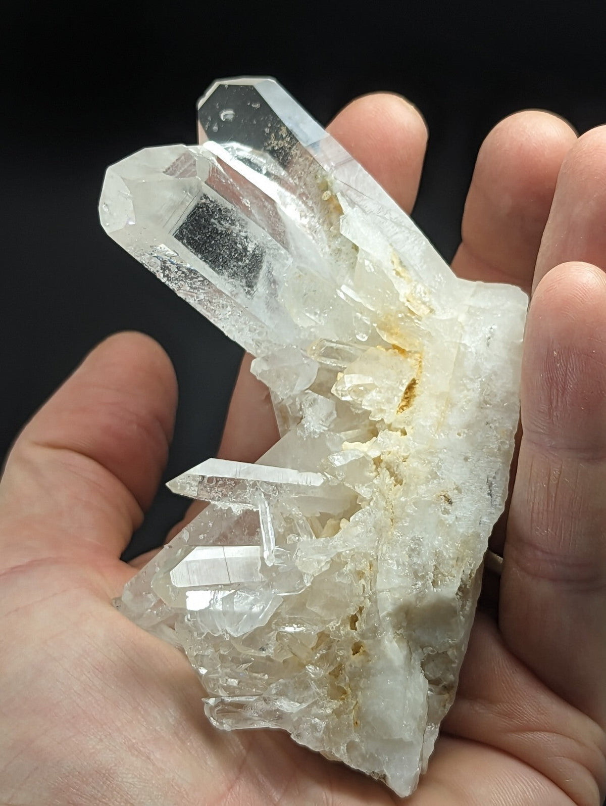 A clear quartz crystal cluster with sharp, faceted points and a translucent body held in a hand.