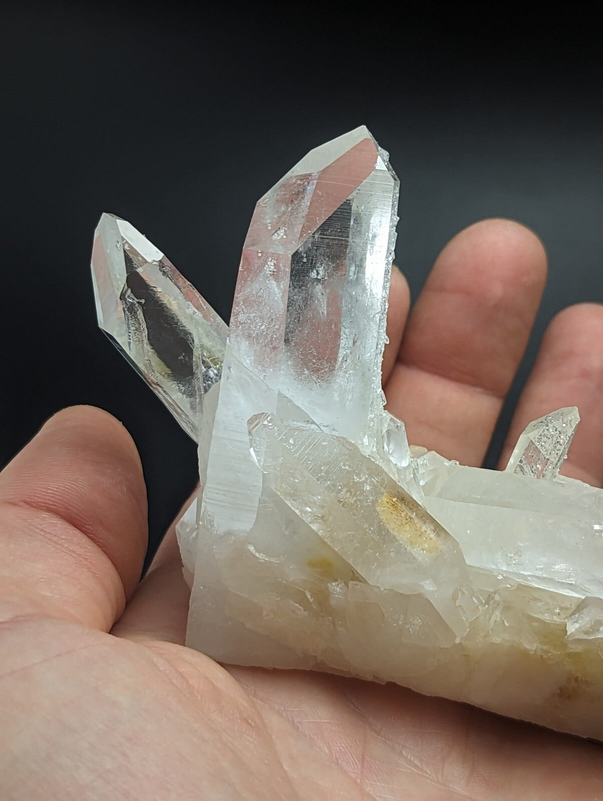 A clear, translucent quartz crystal cluster with sharp, pointed facets and a base that shows subtle yellowish inclusions.