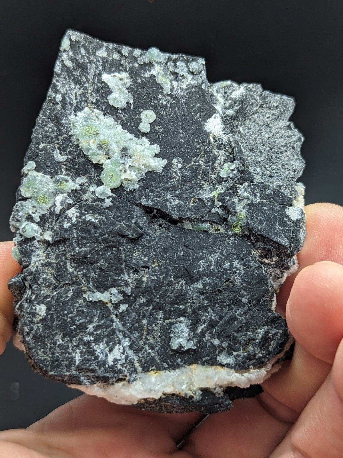 A dark, rough-textured rock specimen featuring clusters of translucent green crystals embedded in its surface.